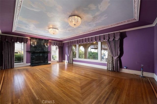 empty room featuring a tray ceiling, crown molding, baseboards, a notable chandelier, and a fireplace