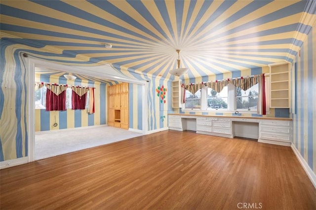 interior space with built in desk, wood finished floors, baseboards, and wallpapered walls