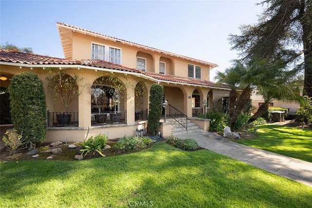 mediterranean / spanish home with a front lawn, a tile roof, stucco siding, and covered porch