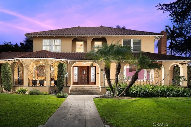 mediterranean / spanish house featuring a tile roof, a front yard, a chimney, stucco siding, and a porch