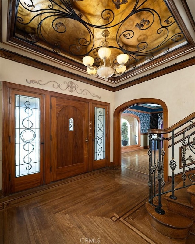 entryway with arched walkways, stairs, ornamental molding, and an inviting chandelier