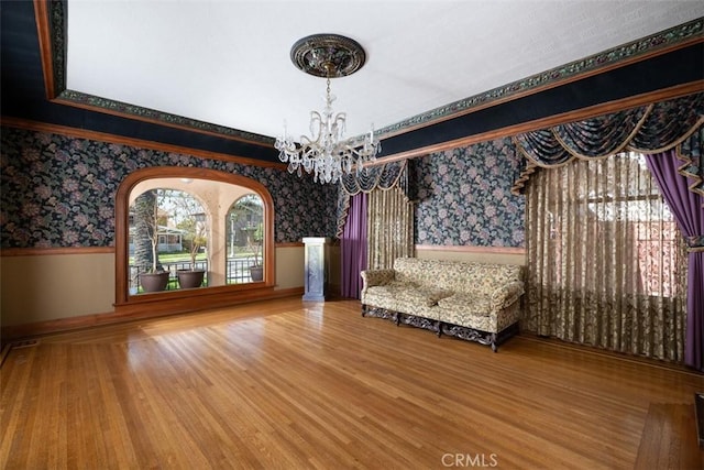 unfurnished room with a wainscoted wall, wallpapered walls, an inviting chandelier, and wood finished floors