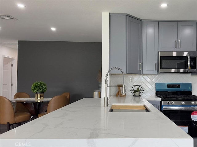 kitchen with tasteful backsplash, gray cabinetry, appliances with stainless steel finishes, a sink, and light stone countertops