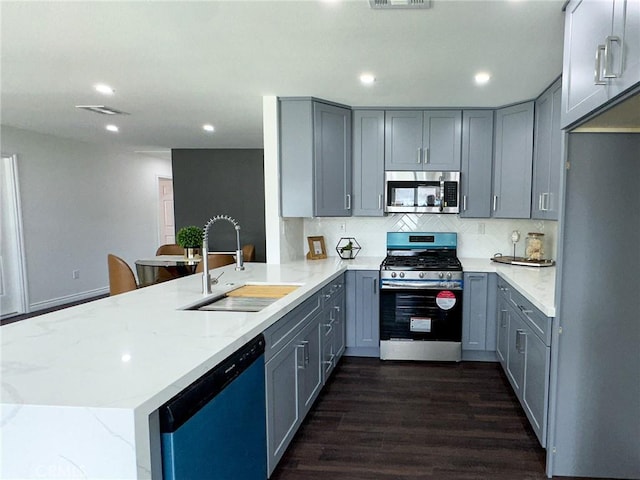 kitchen with decorative backsplash, appliances with stainless steel finishes, a peninsula, gray cabinetry, and a sink