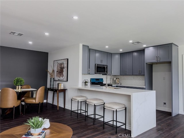 kitchen with visible vents, a peninsula, stainless steel appliances, gray cabinetry, and a sink