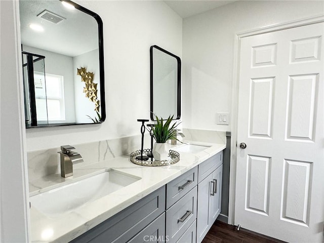 bathroom featuring wood finished floors, visible vents, a sink, and double vanity