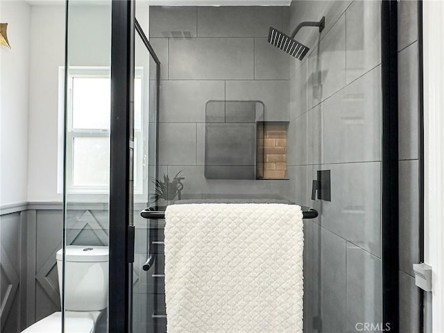 bathroom with toilet, a wainscoted wall, and a shower stall