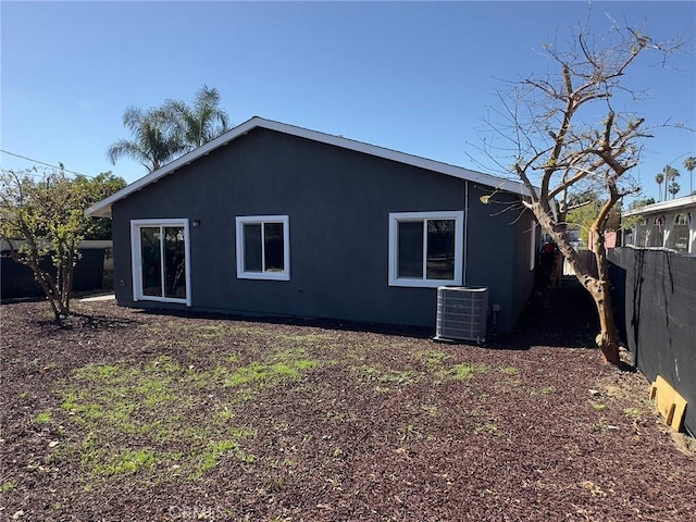 rear view of house featuring stucco siding, fence, and central AC unit