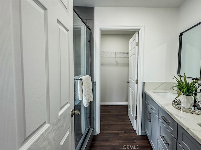 bathroom with double vanity, a spacious closet, a stall shower, a sink, and wood finished floors