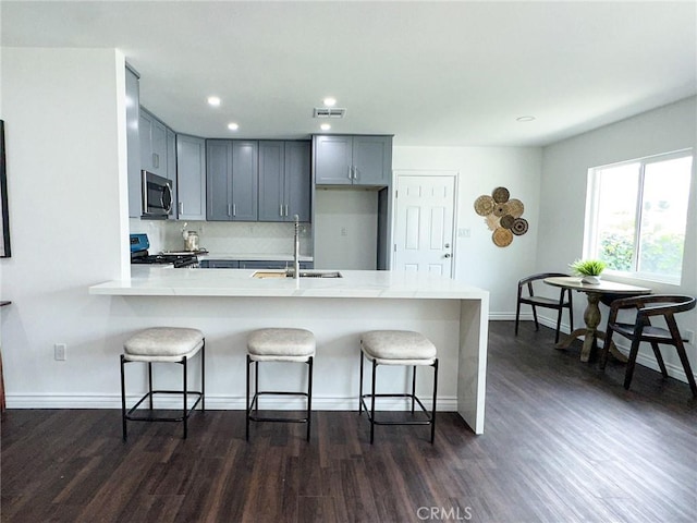 kitchen with gray cabinetry, a peninsula, a sink, appliances with stainless steel finishes, and a kitchen bar