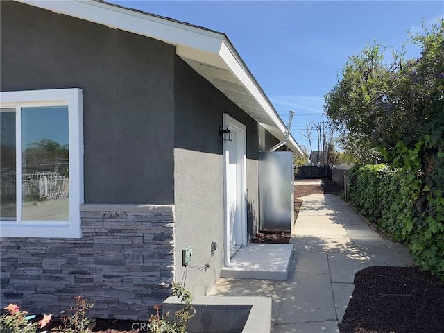 view of side of home with stone siding, a patio area, fence, and stucco siding