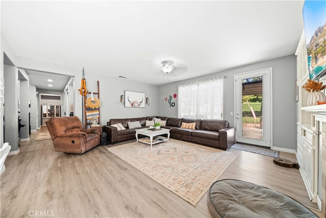 living room featuring light wood-type flooring, a fireplace, visible vents, and baseboards