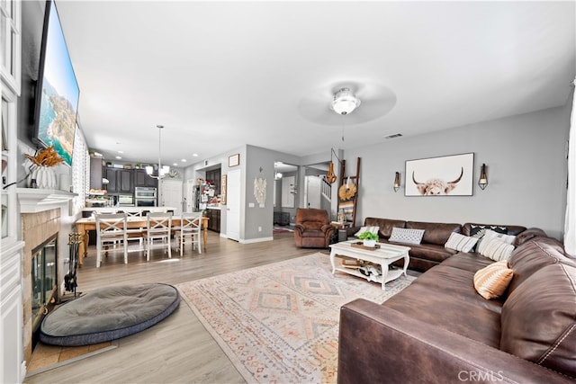 living room featuring baseboards, visible vents, a glass covered fireplace, an inviting chandelier, and light wood-type flooring