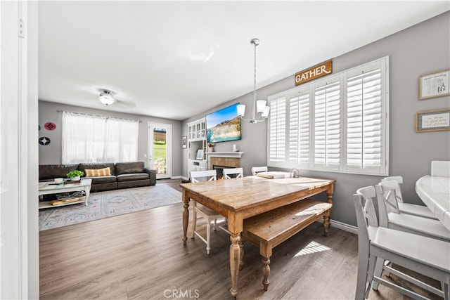 dining space featuring an inviting chandelier, a lit fireplace, baseboards, and wood finished floors