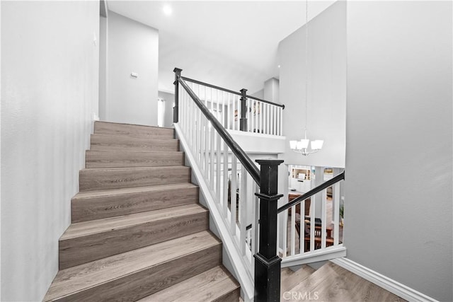 stairway with an inviting chandelier, baseboards, and wood finished floors