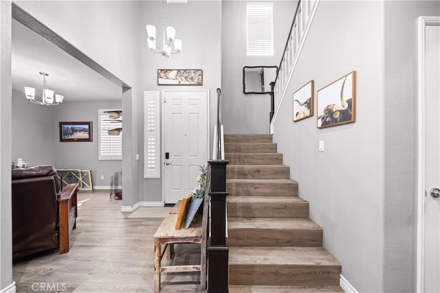 foyer entrance with baseboards, stairway, wood finished floors, and an inviting chandelier