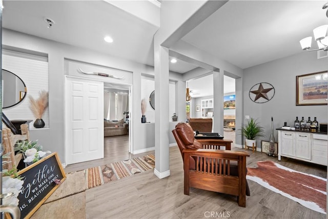 sitting room with baseboards, a glass covered fireplace, wood finished floors, a notable chandelier, and recessed lighting