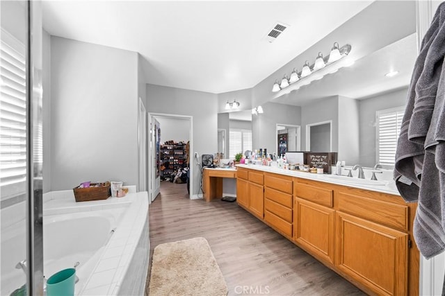 bathroom with a garden tub, double vanity, visible vents, a sink, and wood finished floors