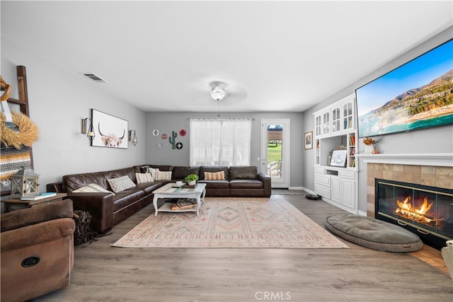 living room with baseboards, visible vents, a tiled fireplace, and wood finished floors