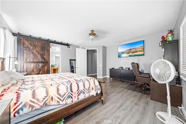 bedroom with a barn door, wood finished floors, a ceiling fan, visible vents, and baseboards