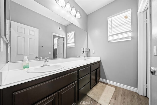 full bathroom with wood finished floors, a sink, baseboards, and double vanity