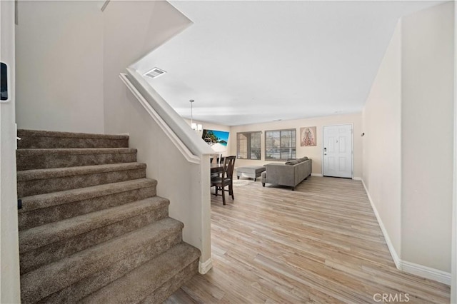 staircase with a notable chandelier, wood finished floors, visible vents, and baseboards