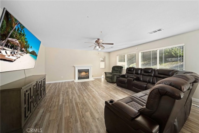 living area featuring a glass covered fireplace, visible vents, baseboards, and wood finished floors