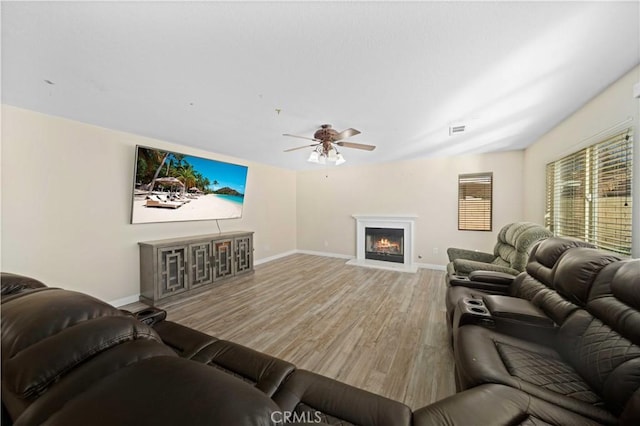 living room featuring a warm lit fireplace, baseboards, visible vents, and light wood finished floors