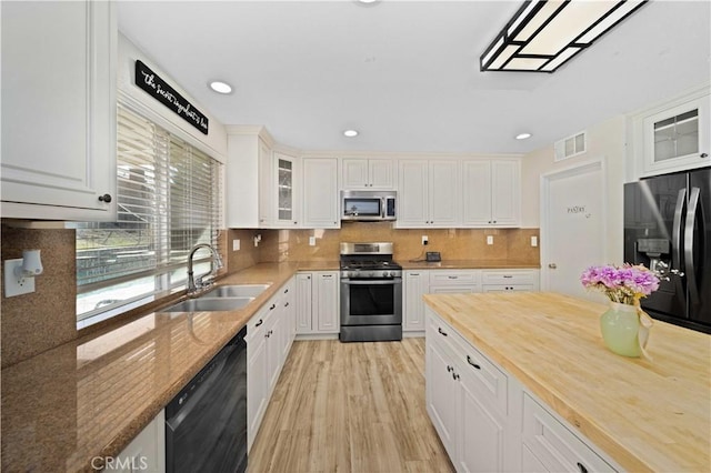 kitchen featuring stainless steel appliances, wood counters, a sink, visible vents, and decorative backsplash