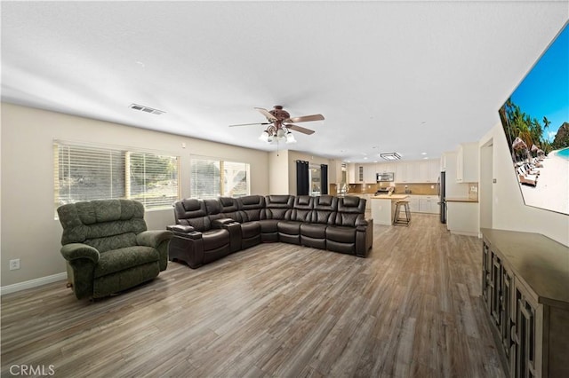 living room with visible vents, ceiling fan, baseboards, and wood finished floors