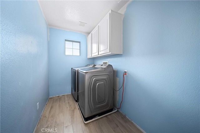 washroom featuring cabinet space, light wood-style floors, and washing machine and clothes dryer