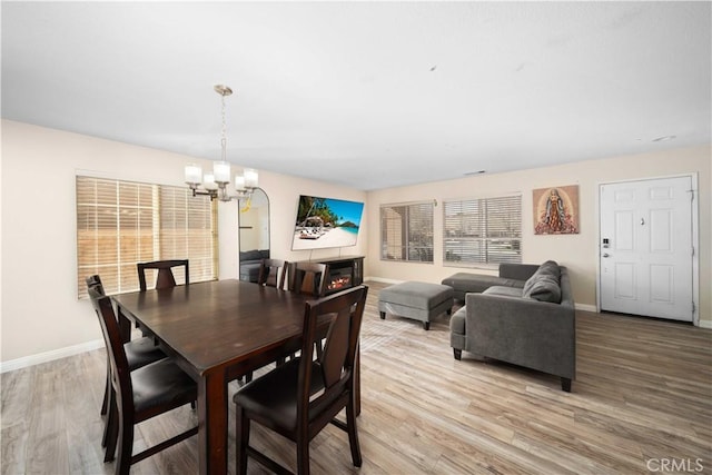 dining space featuring light wood-style floors, a warm lit fireplace, a chandelier, and baseboards