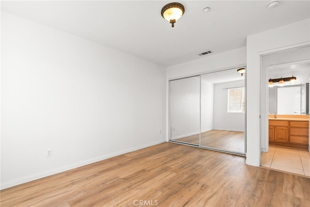 unfurnished bedroom with light wood-type flooring, a closet, visible vents, and baseboards