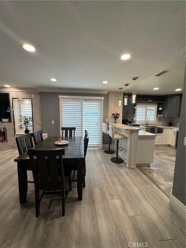 dining room with recessed lighting, visible vents, a textured ceiling, light wood-type flooring, and a warm lit fireplace