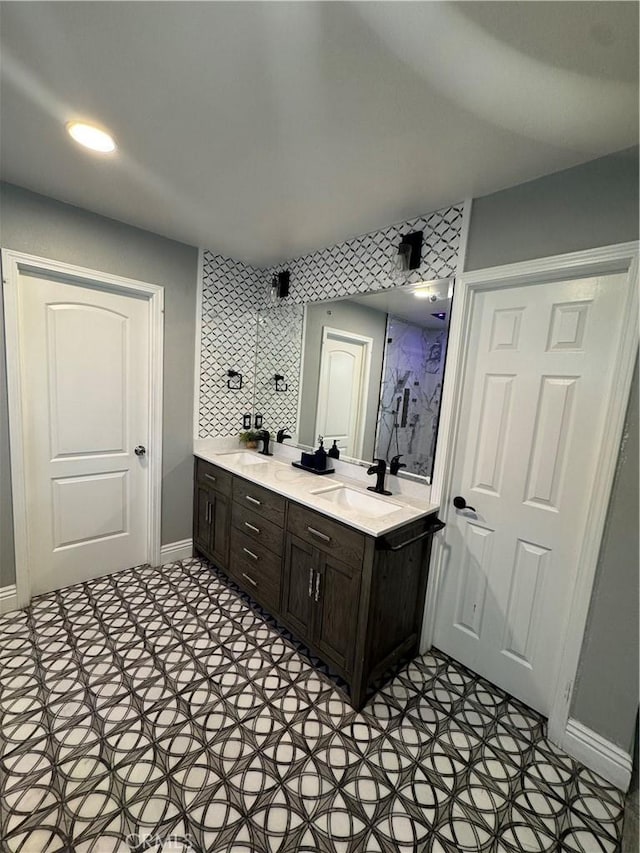 full bath featuring a sink, a shower stall, baseboards, and double vanity