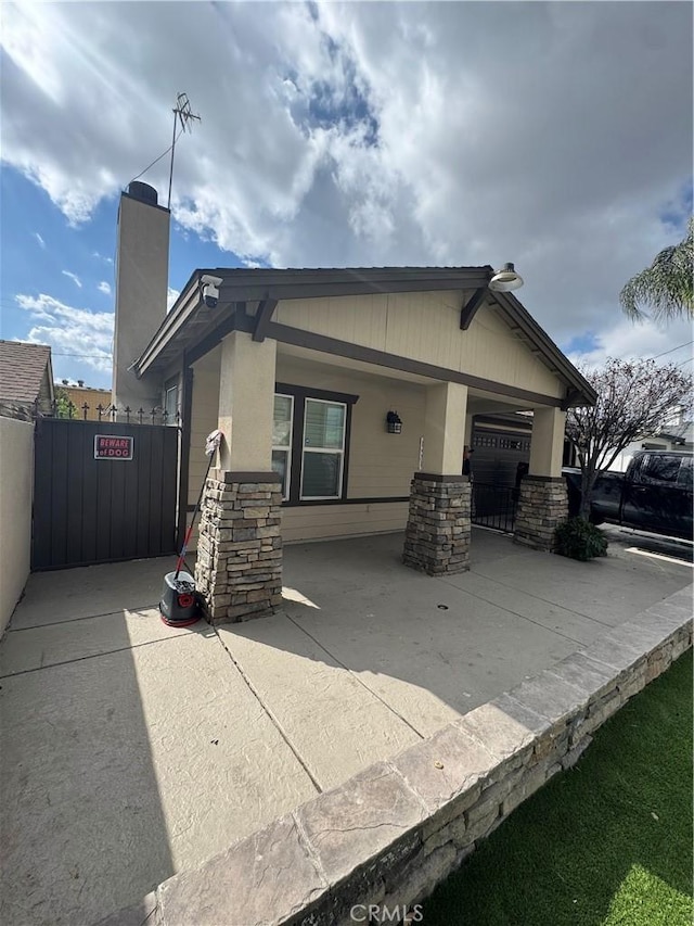 rear view of property with a garage, concrete driveway, stone siding, a chimney, and fence