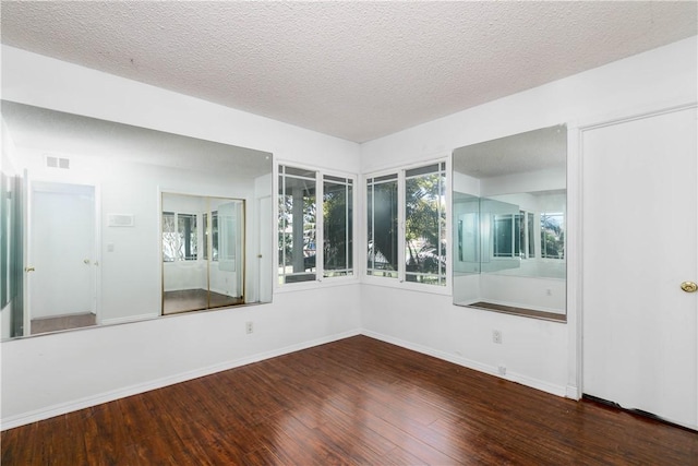 unfurnished room with visible vents, a textured ceiling, baseboards, and wood finished floors