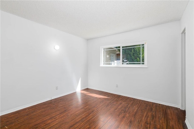 empty room with a textured ceiling, baseboards, and wood finished floors