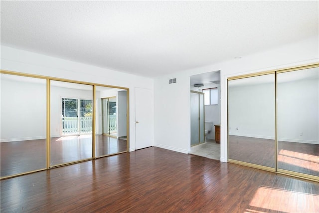 unfurnished bedroom featuring two closets, baseboards, visible vents, and wood finished floors