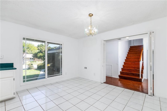 spare room featuring light tile patterned flooring, a notable chandelier, stairway, and a textured ceiling