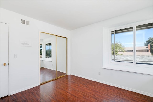 unfurnished bedroom featuring a closet, multiple windows, wood finished floors, and visible vents