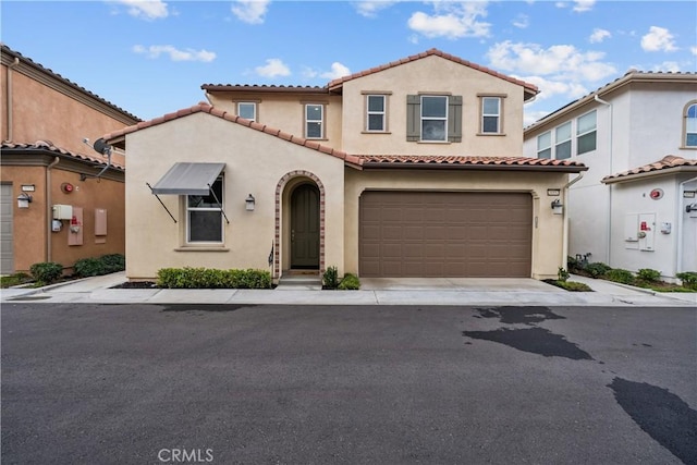 mediterranean / spanish-style home with a garage, driveway, a tiled roof, and stucco siding