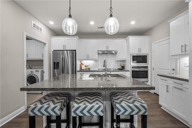 kitchen with a breakfast bar area, appliances with stainless steel finishes, under cabinet range hood, white cabinetry, and a sink