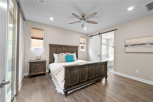 bedroom featuring a barn door, baseboards, dark wood-style flooring, and visible vents