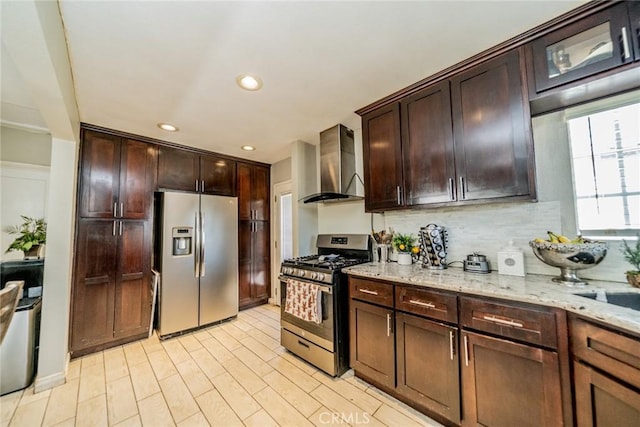 kitchen with light stone counters, light wood-style flooring, appliances with stainless steel finishes, decorative backsplash, and wall chimney exhaust hood