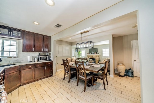 kitchen with dark brown cabinetry, visible vents, decorative backsplash, stainless steel microwave, and a sink