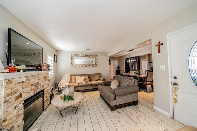 living room featuring recessed lighting, a stone fireplace, light wood-style flooring, and baseboards