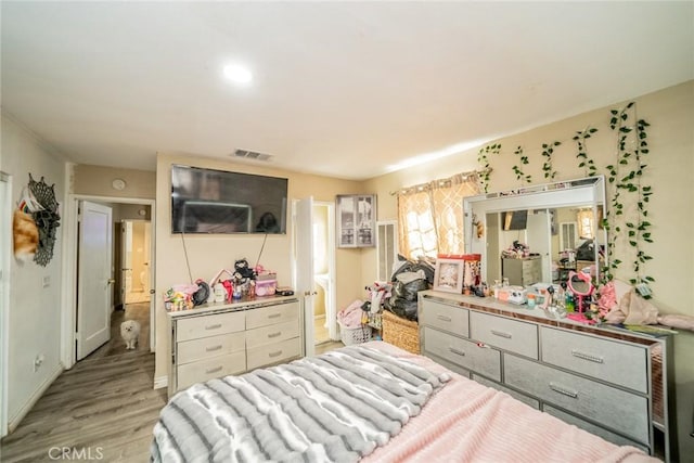 bedroom featuring light wood-style floors, baseboards, visible vents, and connected bathroom