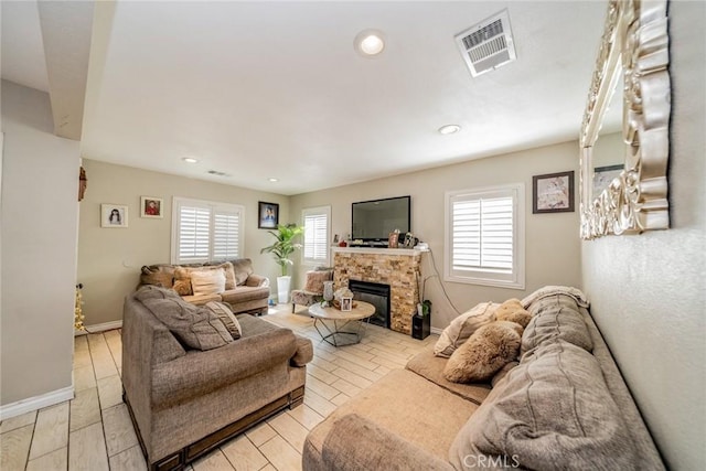 living room featuring a wealth of natural light, visible vents, a stone fireplace, and baseboards