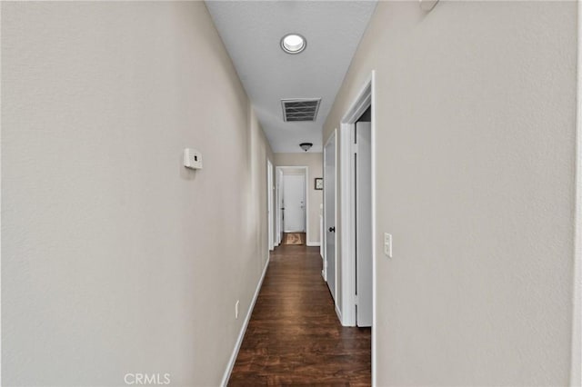 hall featuring dark wood finished floors, visible vents, and baseboards